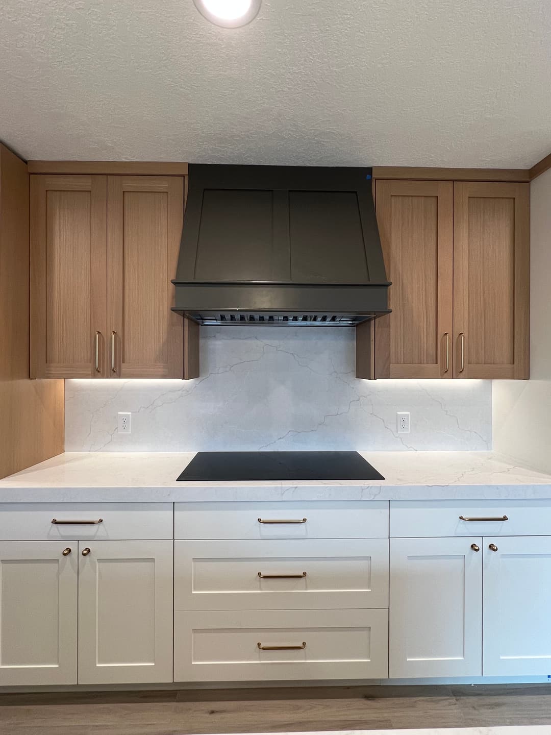 Modern kitchen with wood and white cabinets, marble backsplash, and a sleek range hood.