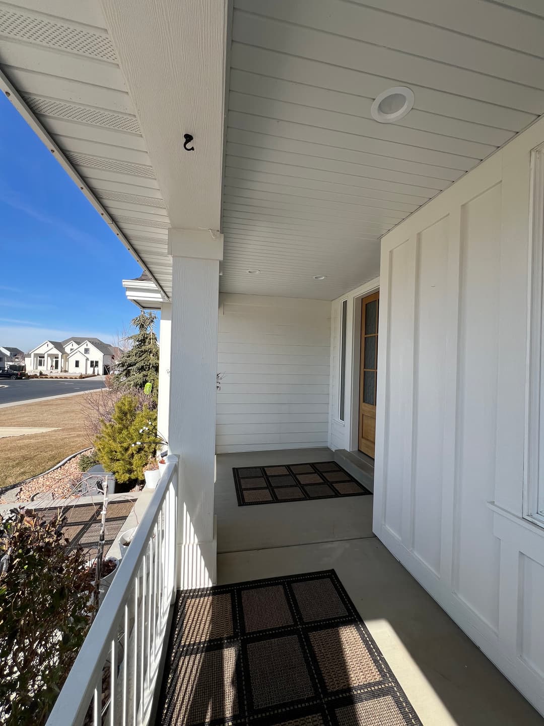 Welcoming front porch with two mats and a wooden door, featuring a clear blue sky backdrop.