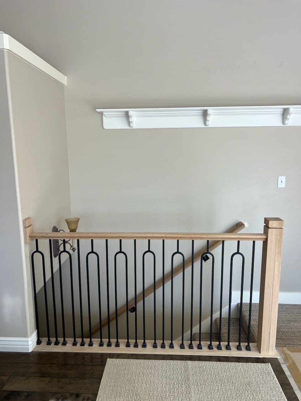 Modern wooden stair railing with black metal balusters and neutral wall colors.