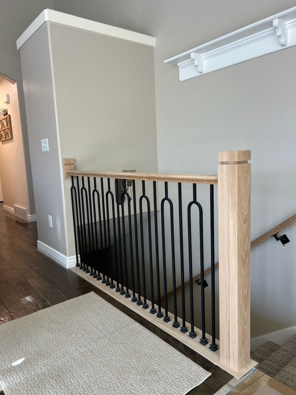 Modern wooden and black metal stair railing in an interior hallway with beige walls.