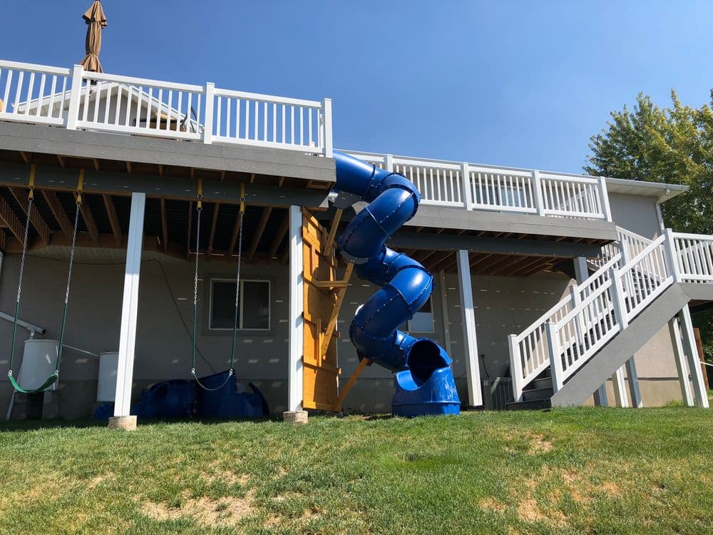 Blue spiral slide attached to raised deck in backyard with green grass and clear sky.
