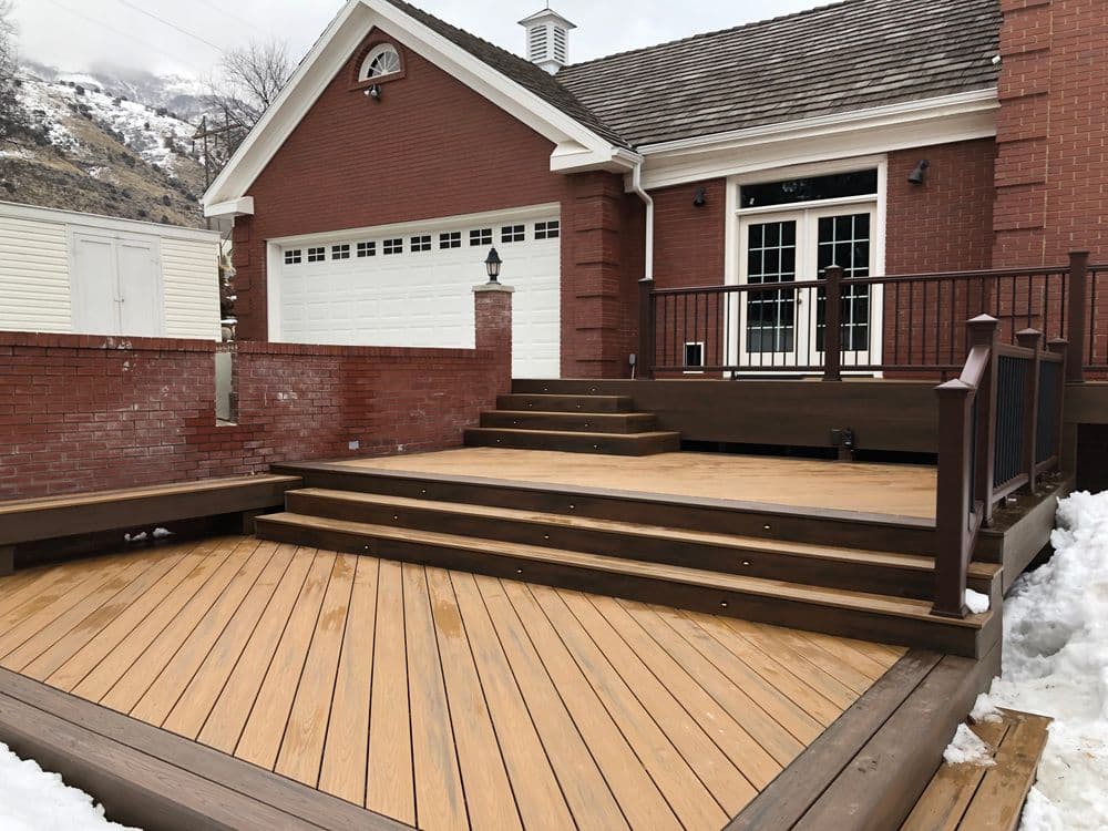 Modern home exterior with wooden deck, steps, and snowy landscape.