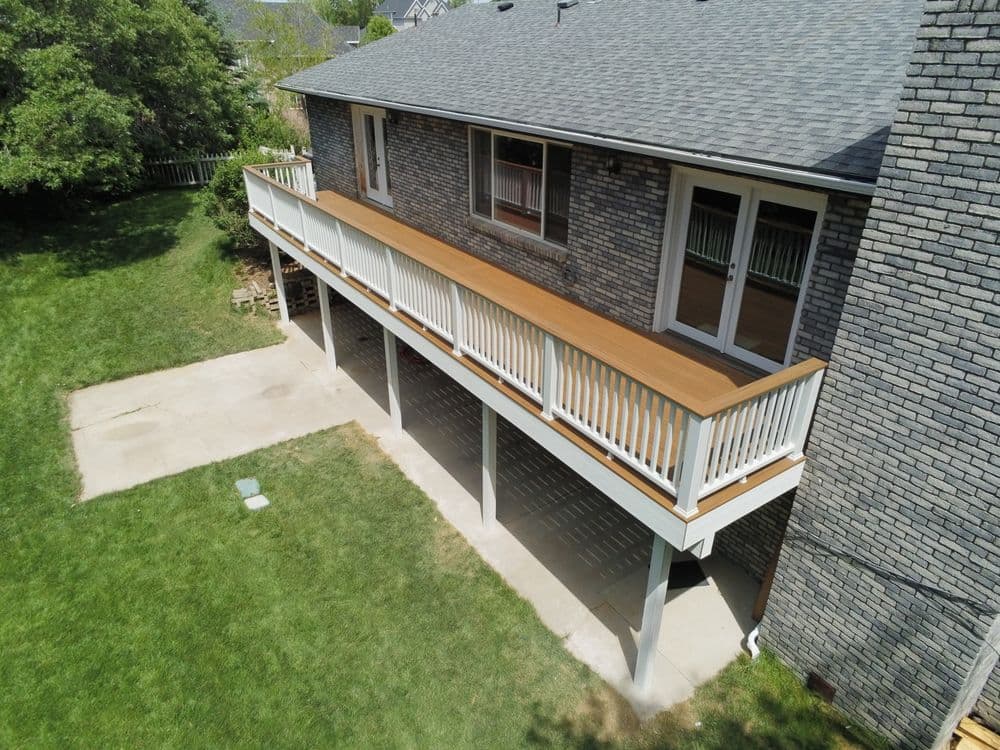 Modern elevated deck with wooden railing and spacious undercroft, surrounded by green lawn.
