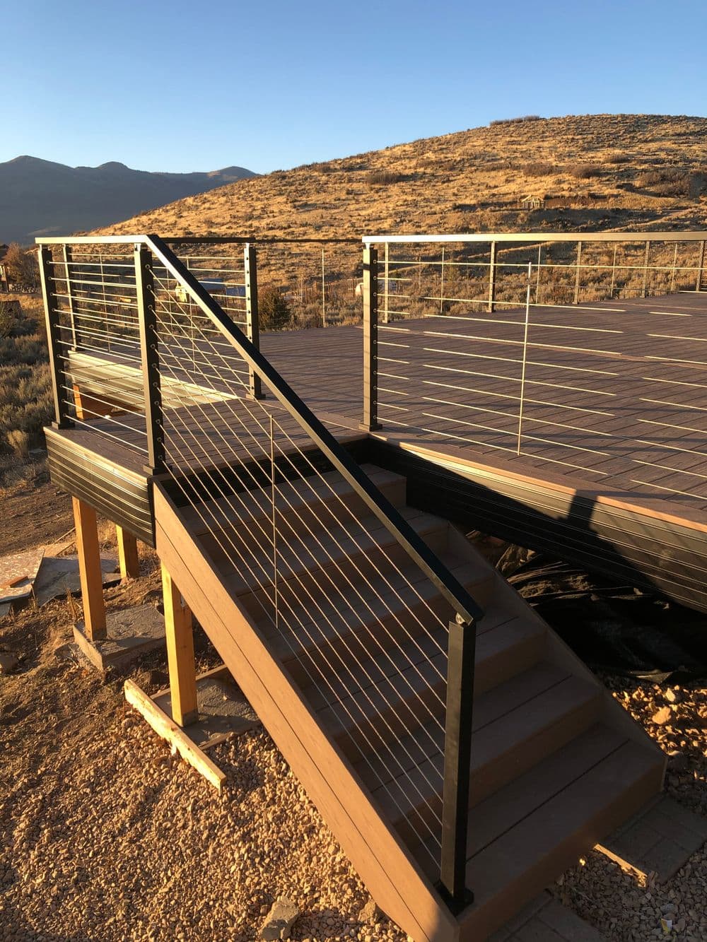 Modern wooden deck with cable railing and stairs, set against a rugged mountain backdrop.