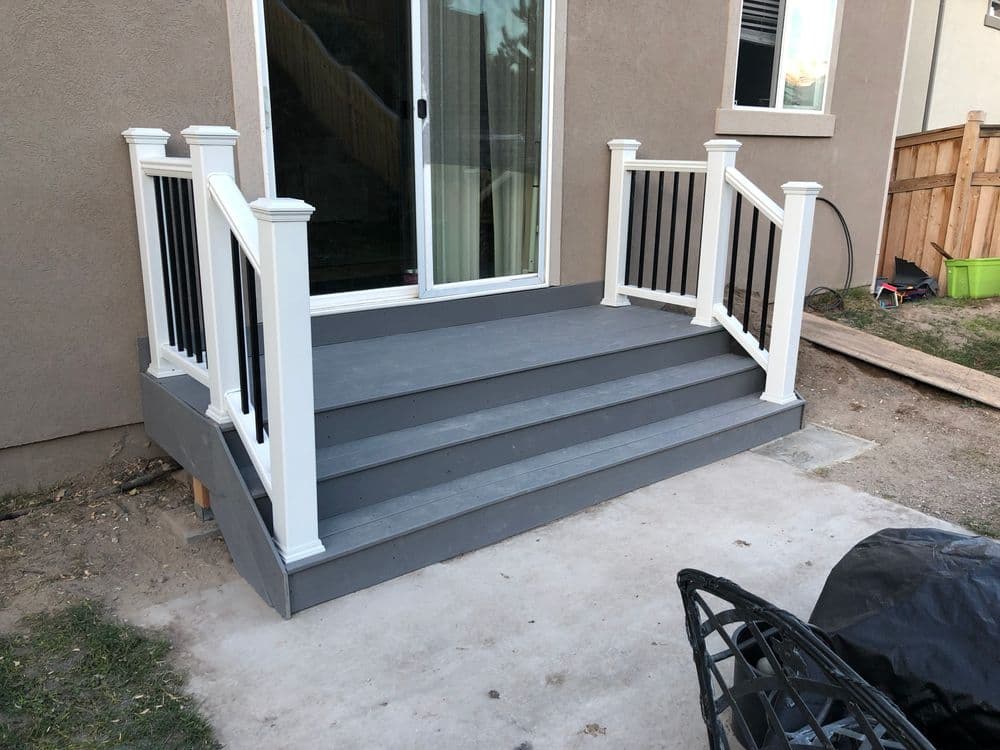 Modern gray deck with white railings and steps leading to a sliding glass door entrance.