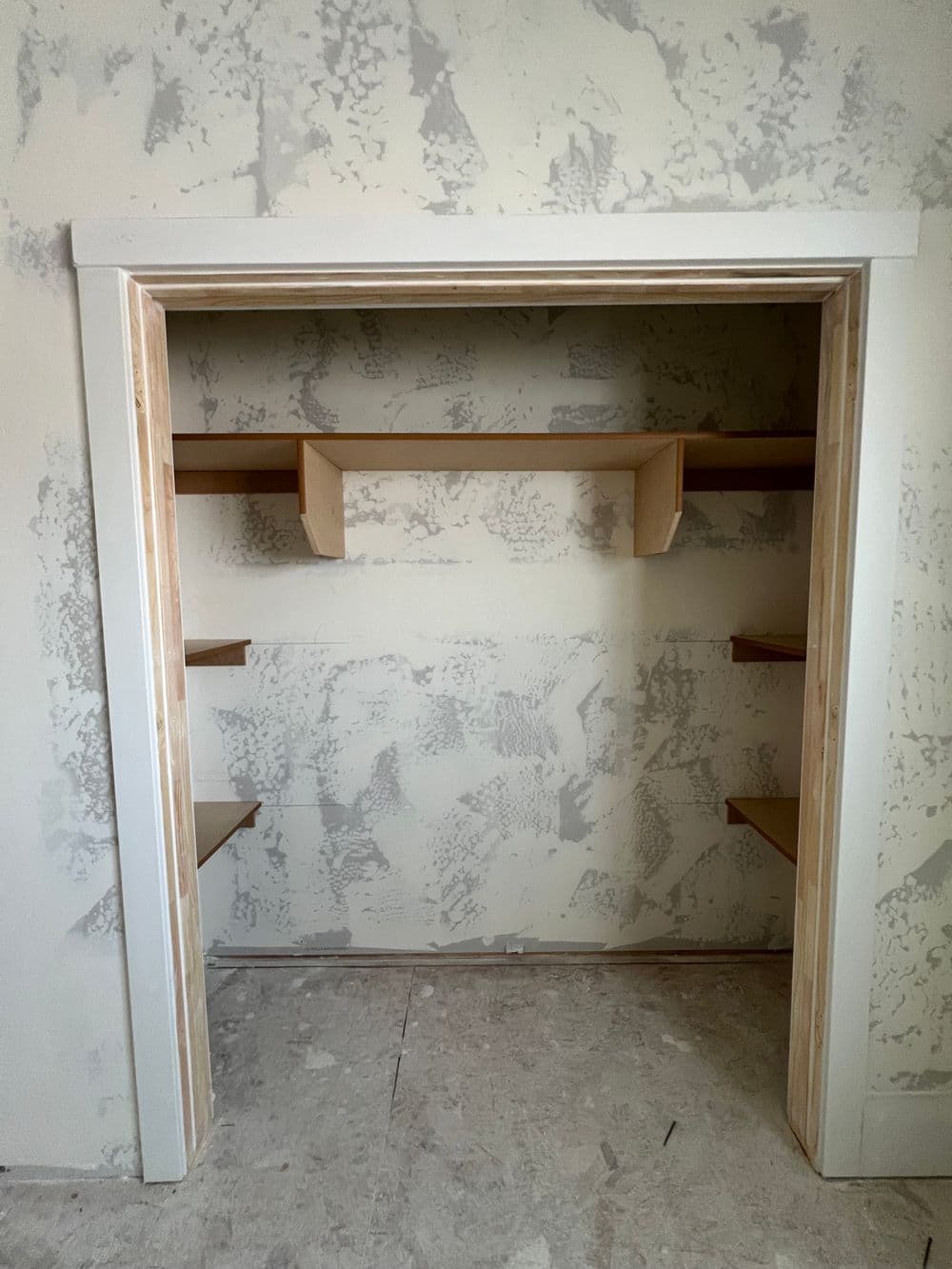 Empty closet with unfinished walls and wooden shelves, showcasing minimal storage space.