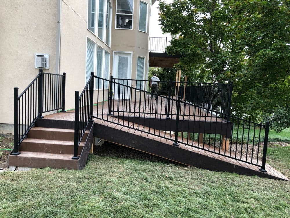 Black metal railings on a wooden deck with stairs and a wheelchair-accessible ramp.