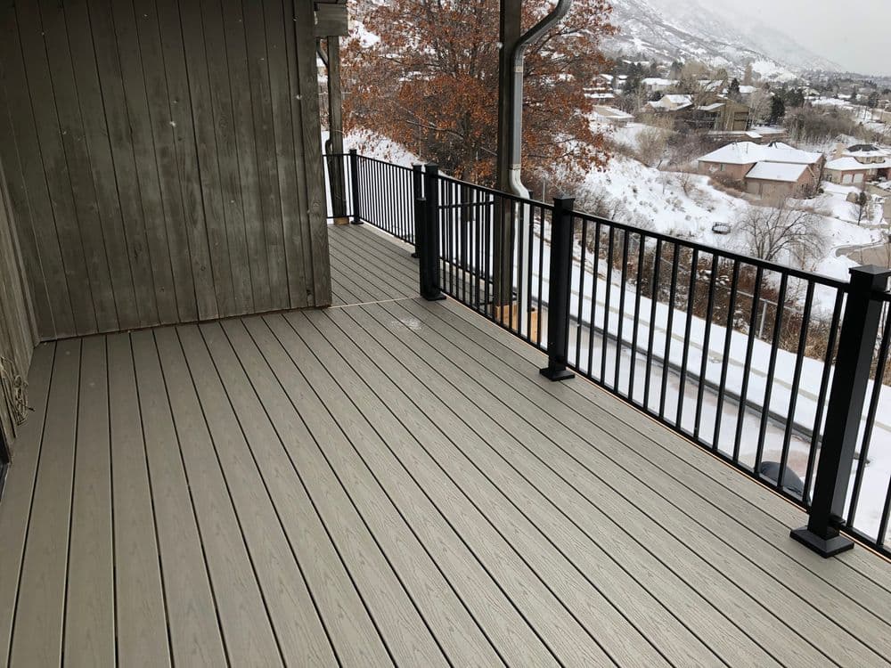 Composite decking on a balcony with black railing, overlooking snowy mountains and homes.